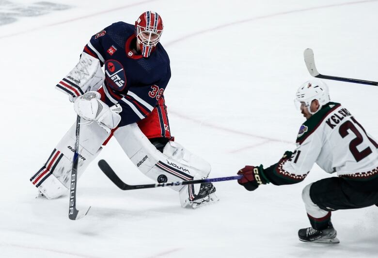 A hockey player skates toward a goaltender as the puck flies in the air.