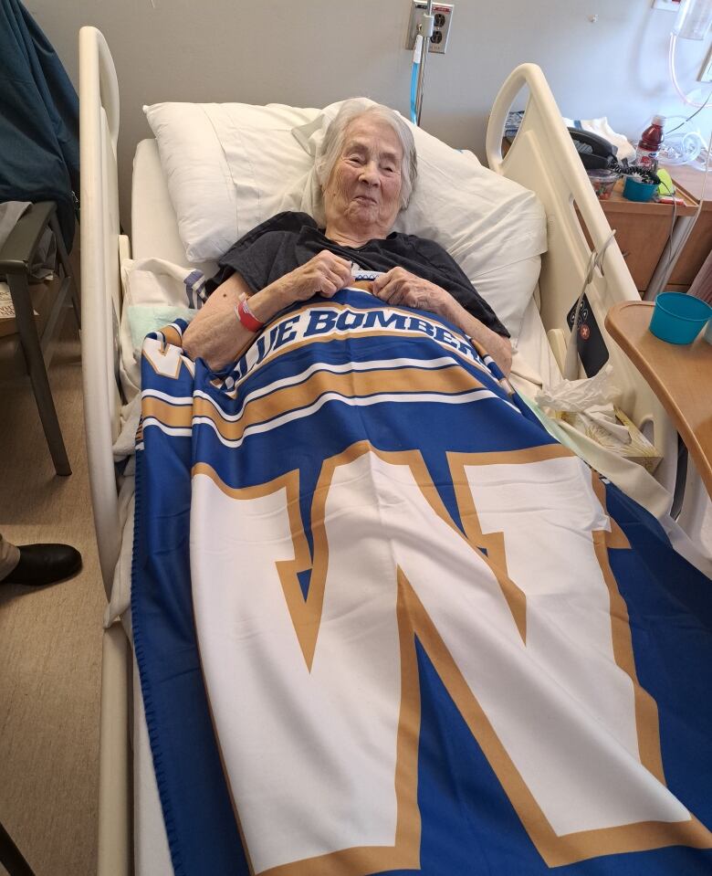 A woman with grey hair lays in a hospital bed with a football team's flag draped over her.