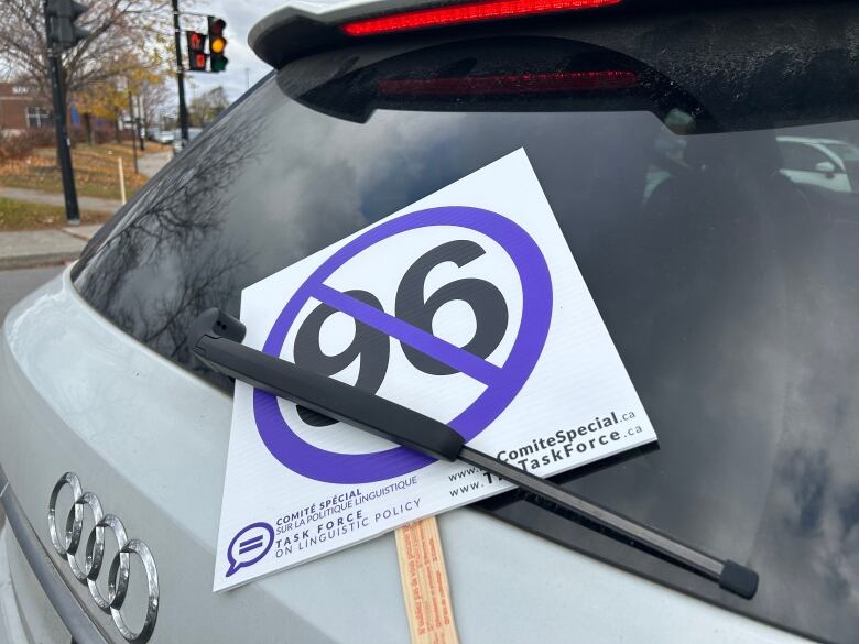 A sign with the number 96 with a slash through it wedged between the back wipers of a car. 