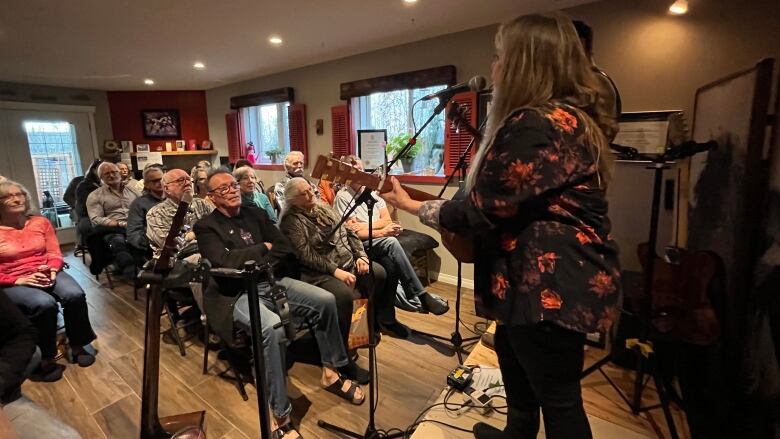 a room full of people while two people with guitars and microphones stand at the front