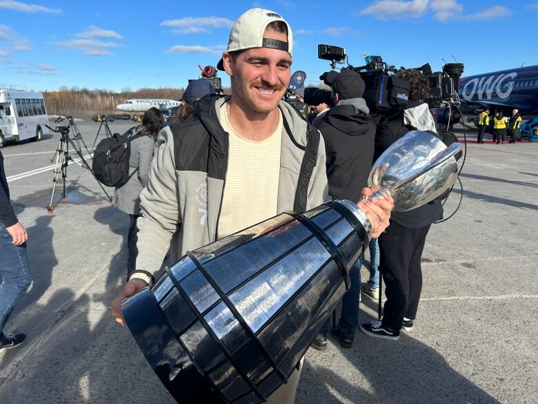 Cody Fajardo holding the Grey Cup on tarmac. 