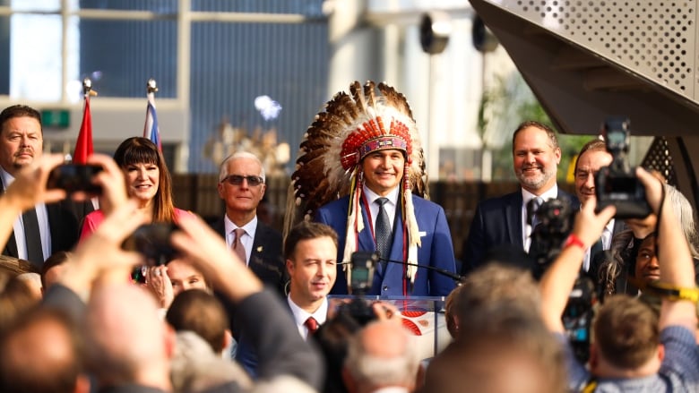 A politician in a blue suit and headdress smiles while flanked by others in his party at a government swearing in ceremony.