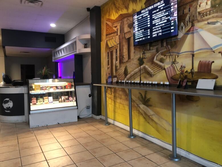 A counter and a shelf filled with magic mushroom products and a TV with the full product line and prices