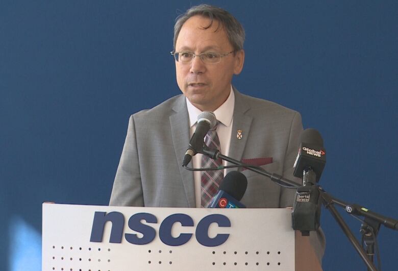 A man with glasses stands at a podium.