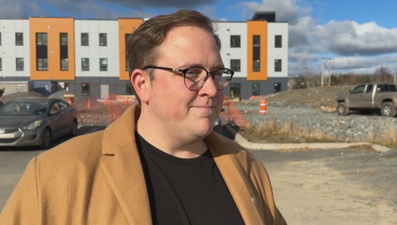 A person with glasses stands in front of a construction site.