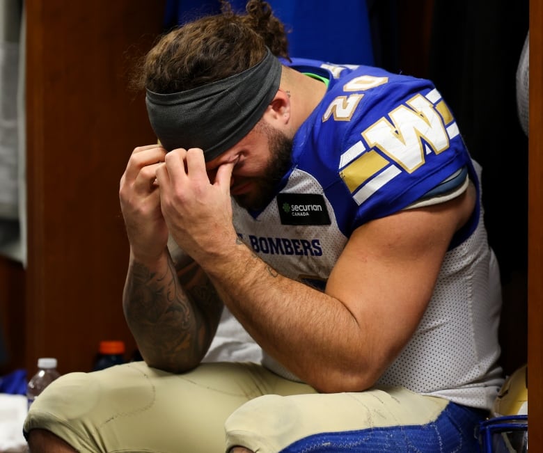 Man in football uniform, without helmet, sits with his head in his hands.