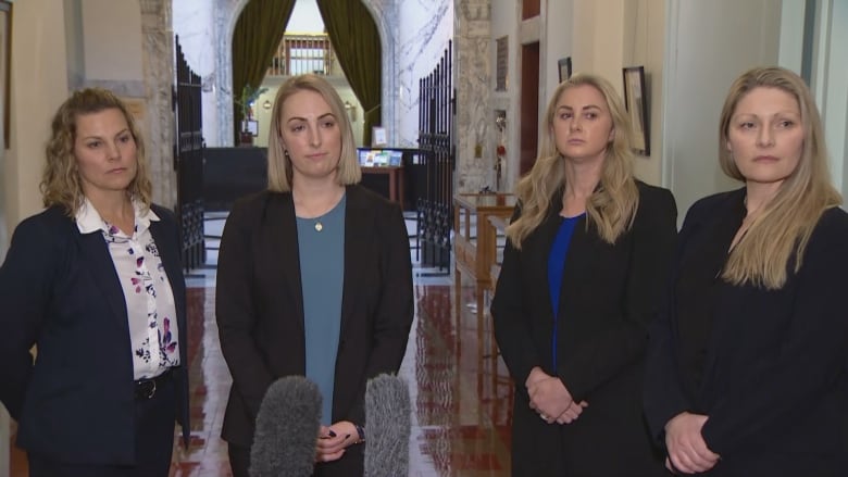 A group of blonde woman hold a news conference in the hallway of a legislative building.