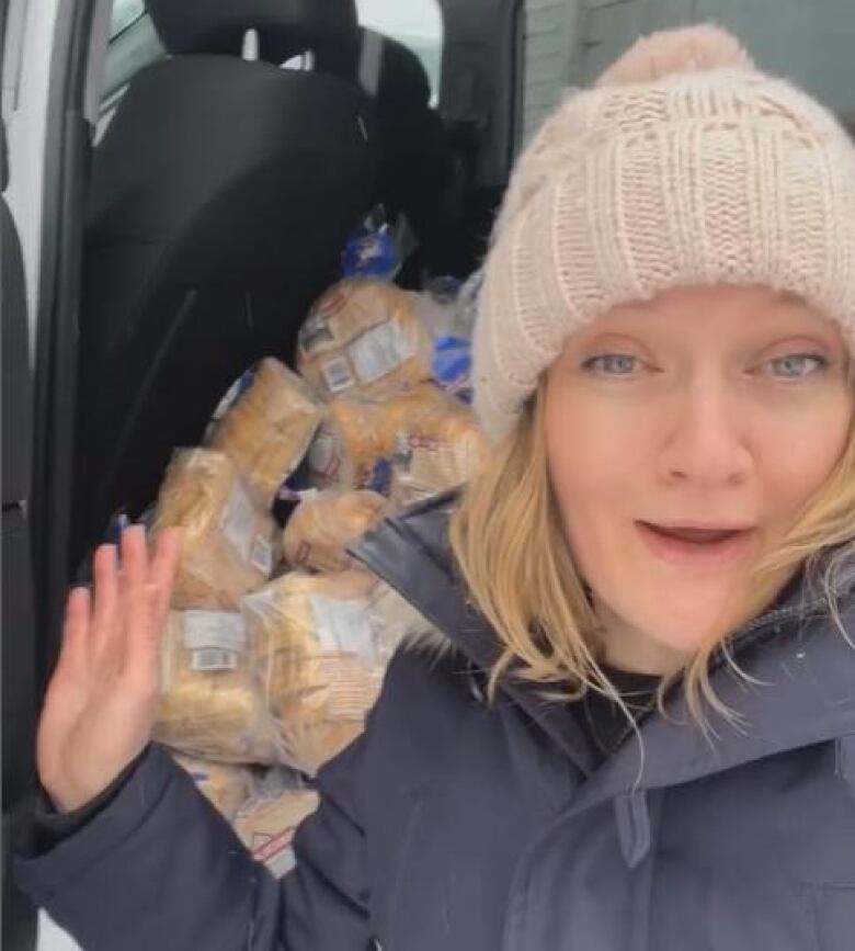 Woman sitting in the back of a car with piles of bread to deliver