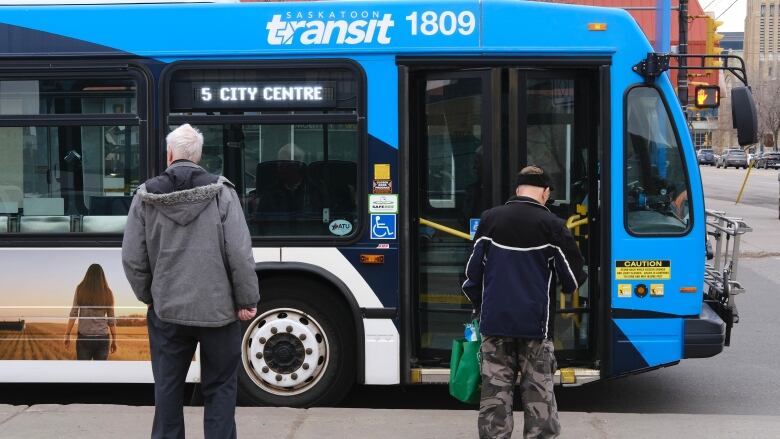 Two people stand with only their backs visible and a bus is stopped in front of them