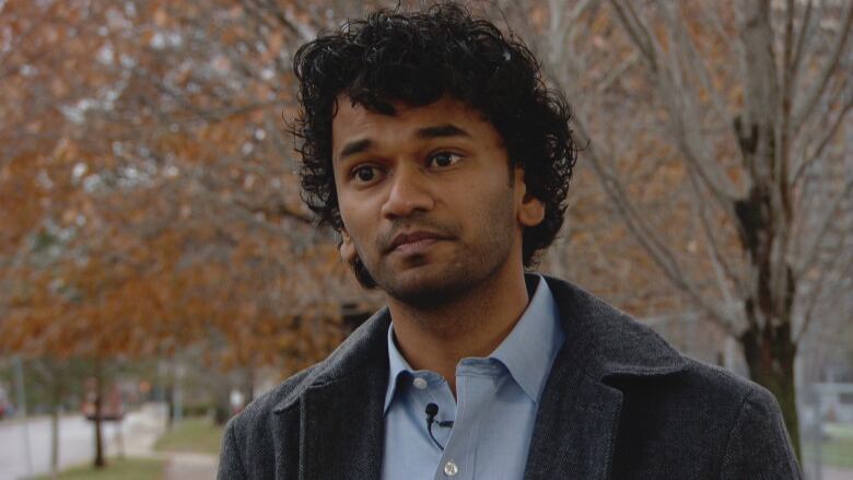 Man wearing brown coat and blue shirt looks ahead on a city street.