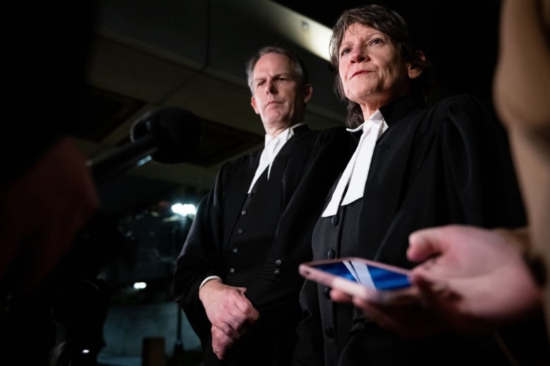 Two crown prosecutors speak to reporters outside of a courthouse.