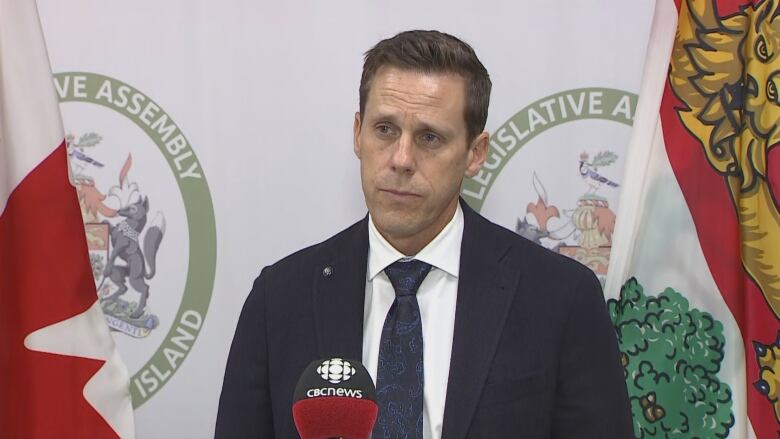  A man stands in front of a microphone waiting to answer questions from reporters. 