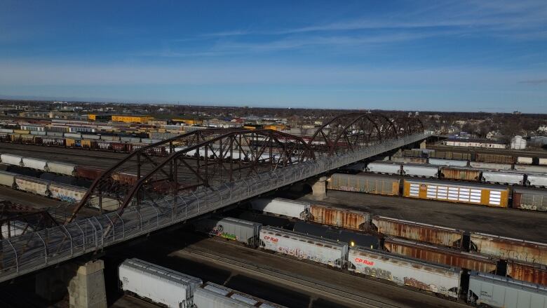 A drone shot shows a bridge over a rail yard.