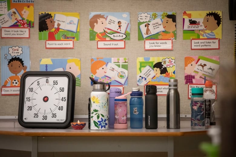 Water bottles on a desk in a school, with language learning cards pinned on a board in the background for children's sake.