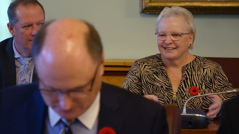 A man and a woman sitting beside each other. A man, looking down, sits in front of them.