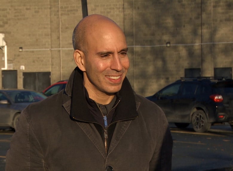 A smiling man stands in a parking lot.