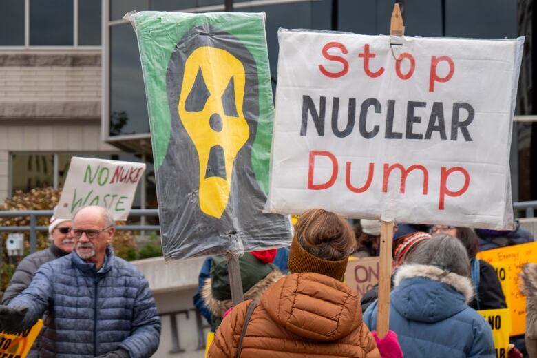 People wearing winter jackets seen from behind holding signs. 