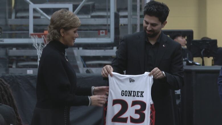 A man hands a basketball jersey to a woman.