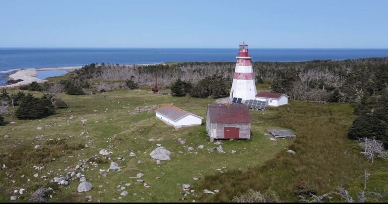 An aerial view of an octagonal wooden lighthouse with three smaller structures and a solar panel nearby. 