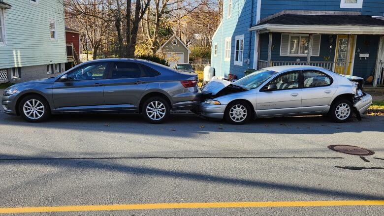 two vehicle's parallel parked are damaged. The hood on the rear vehicle is bent and the bumper is falling off. 