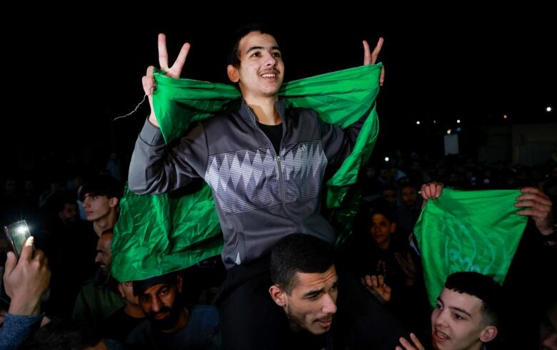 A young smiling Palestinian on a man's shoulder surrounded by a crowd after he's released from an Israeli military prison.