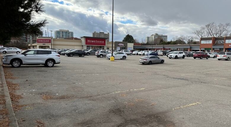 A wide-angle view of a parking lot partly filled with vehicles, with a shopping plaza in the background.  