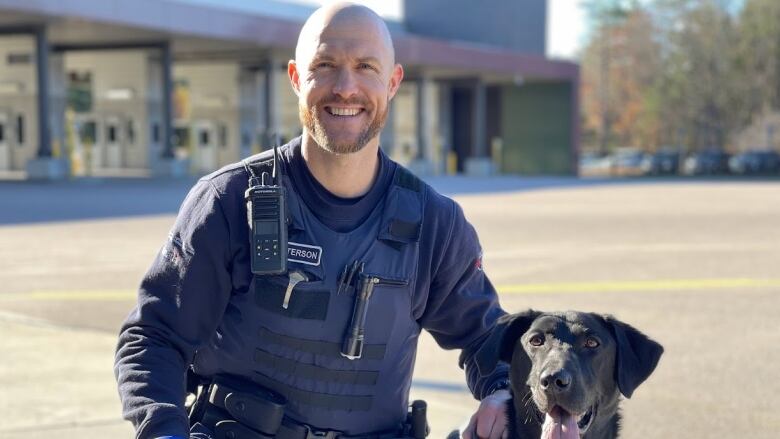 A uniformed man kneels with a black dog.