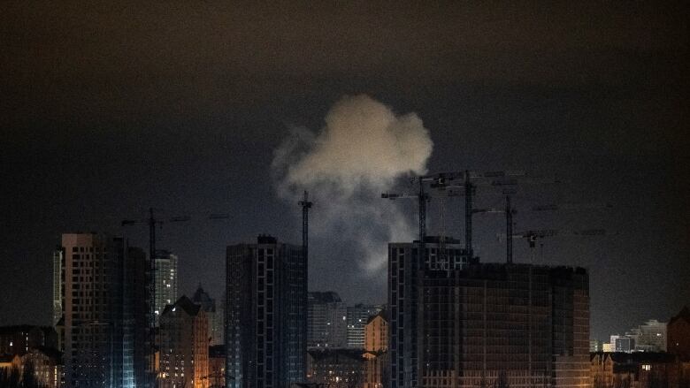 Smoke rises behind a city skyline at night.