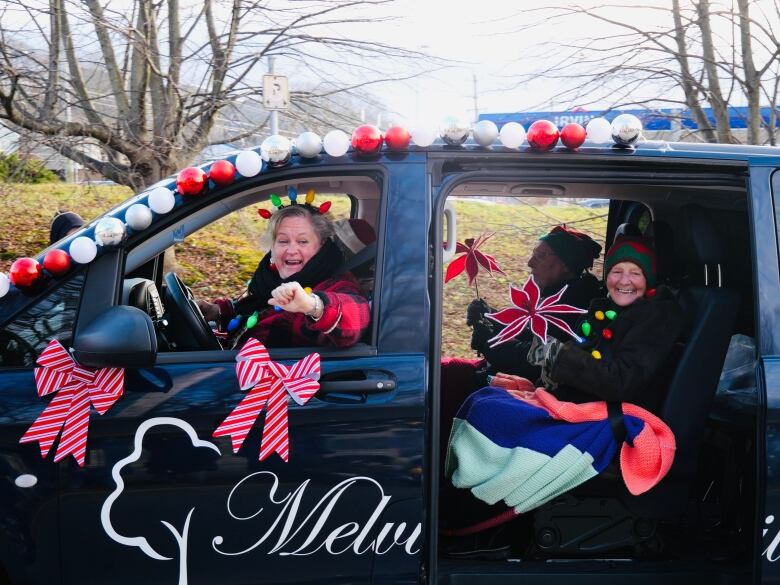 Two people wave from inside a black van decorated in red and white ornaments.