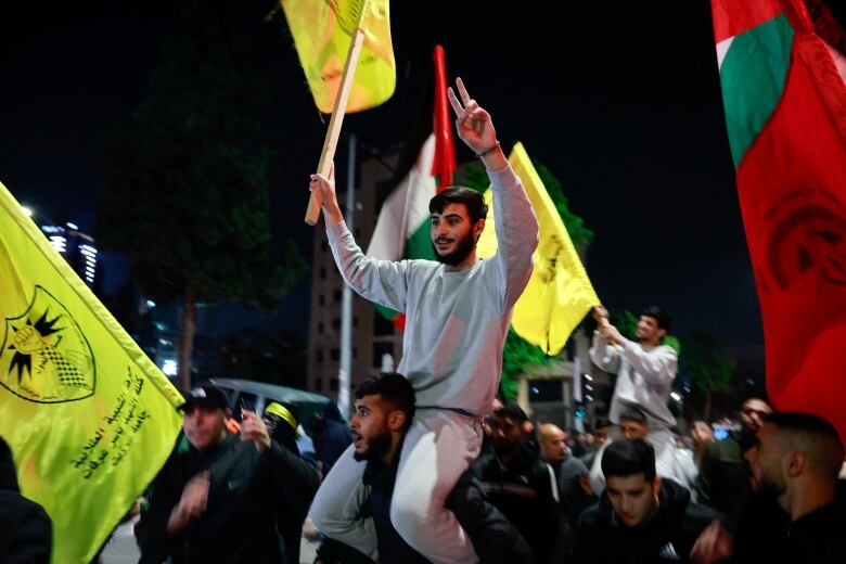 A person gestures with the the peace sign as they sit atop a person's shoulders.