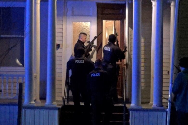 Four armed police offices stand on a home's porch at the front door.