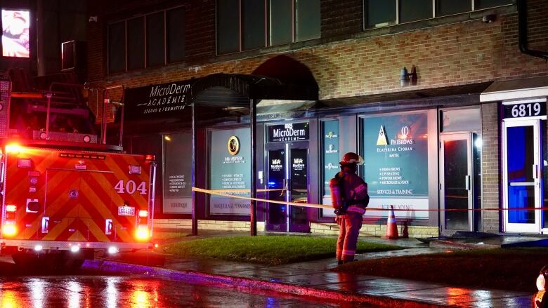 A firefighter standing outside a building blocked off by police tape near a fire truck. 