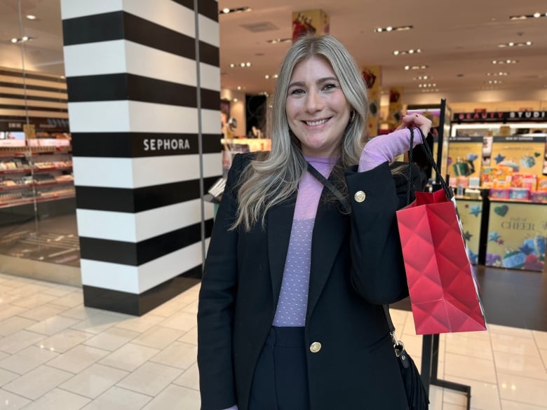 A woman with blonde hair and a blazer is pictured holding a red shopping bag.