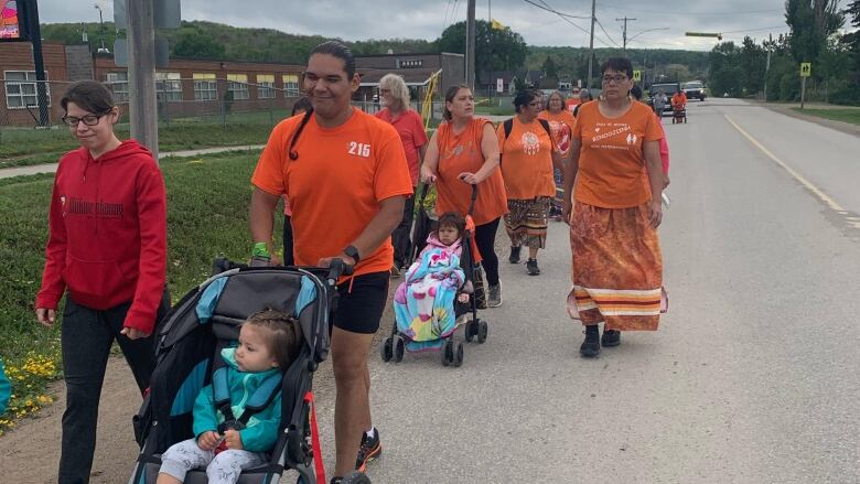 A group of people wearing orange t-shirts walk in the streets.