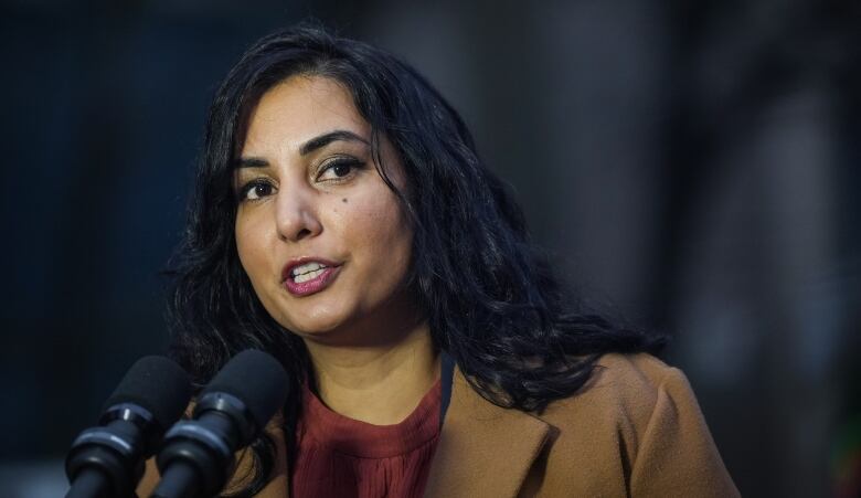 A South Asian woman speaks to a pair of mics.