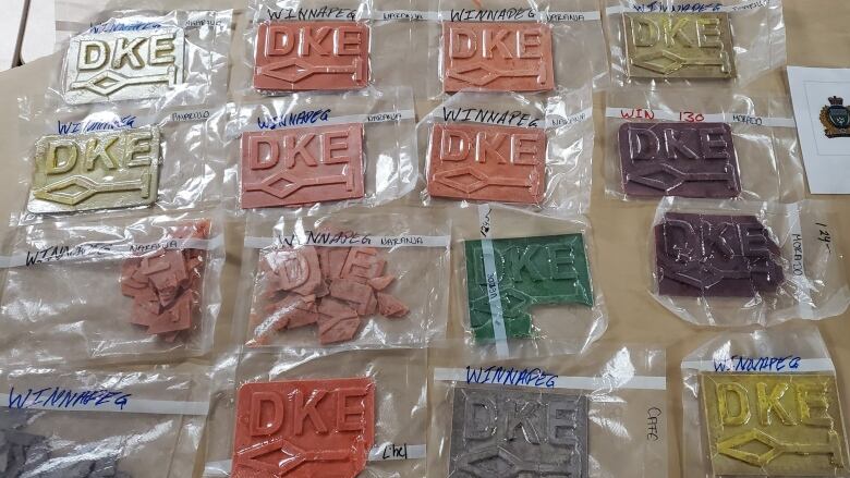 About 16 packages of colourful fentanyl, with the lettering 'DKE' etched in the top of each square piece, is laid out on a table.