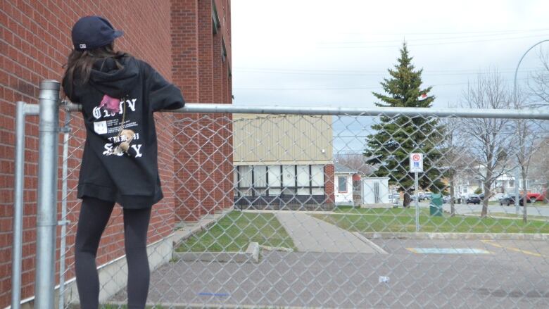 A student stands up against a fence.