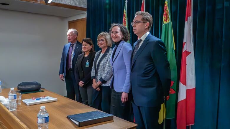 A group of five people stand in front of the Saskatchewan and Canadian flags. 