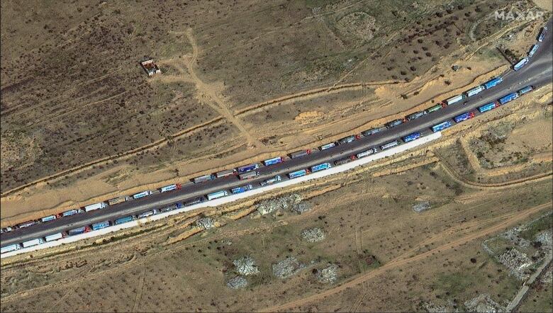 An aerial view shows trucks lined up on a road.