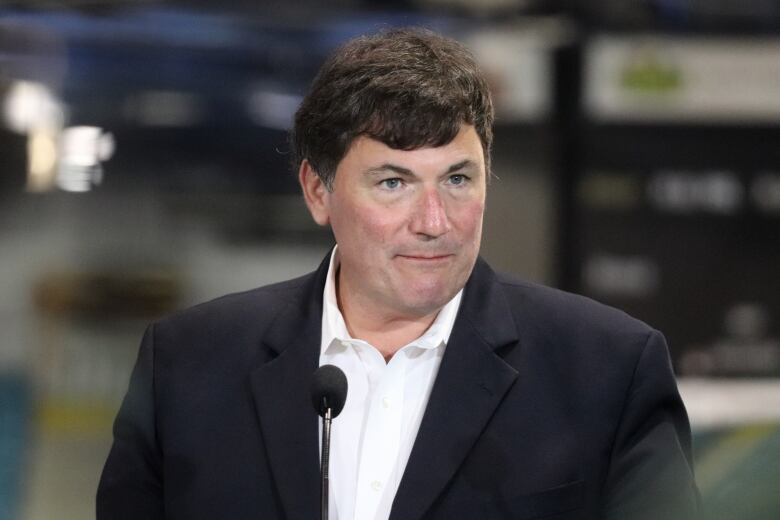 A white man wearing a black jacket speaks at a news conference.