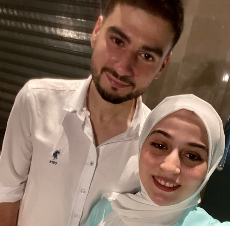 Man in white button up shirt standing next to woman in white headscarf and light blue shirt.