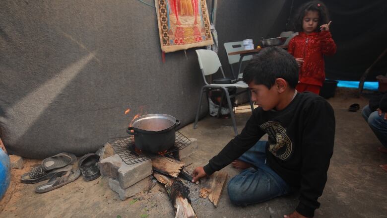 A boy tends to a fire inside a tent at a temporary efugee camp.