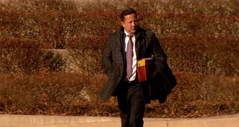 Man in a dark suit and tie with a file folder under his arm. 