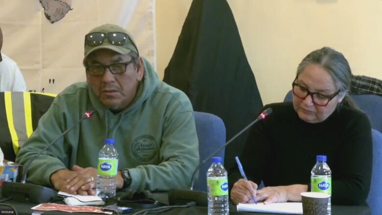 A Man in a green sweaters sits at a table. A woman in a black sweater sits beside him. 