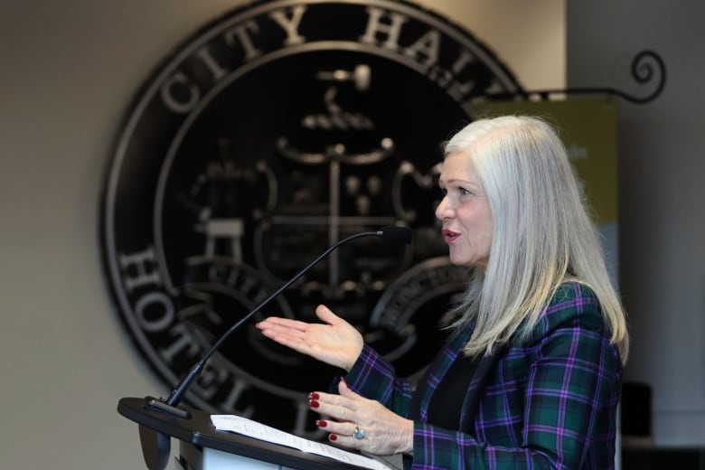 A side profile of a woman in a plaid jacket speaking at a podium. 