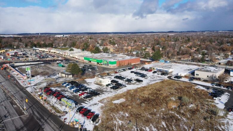 Aerial view of an overgrown vacant lot and vehicles parked, with a light dusting of snow on the ground.    