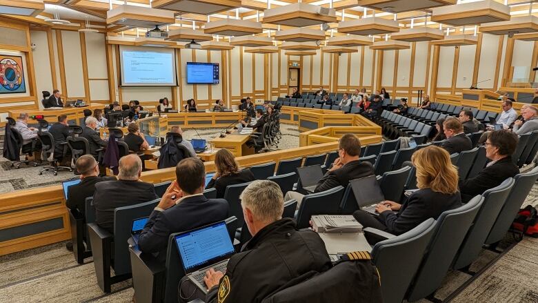 council chambers with some chairs filled and majority empty