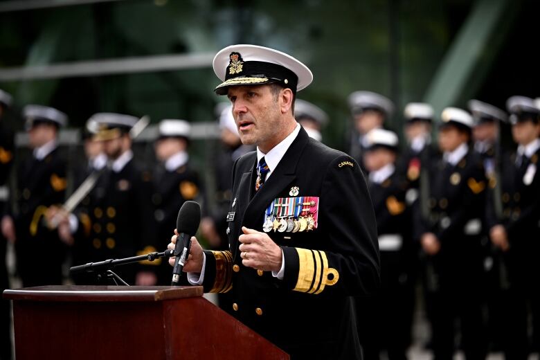 A man in a naval uniform speaks at a podium.