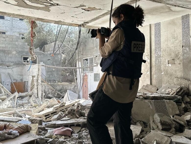 Woman standing on top of rubble holding a camera.