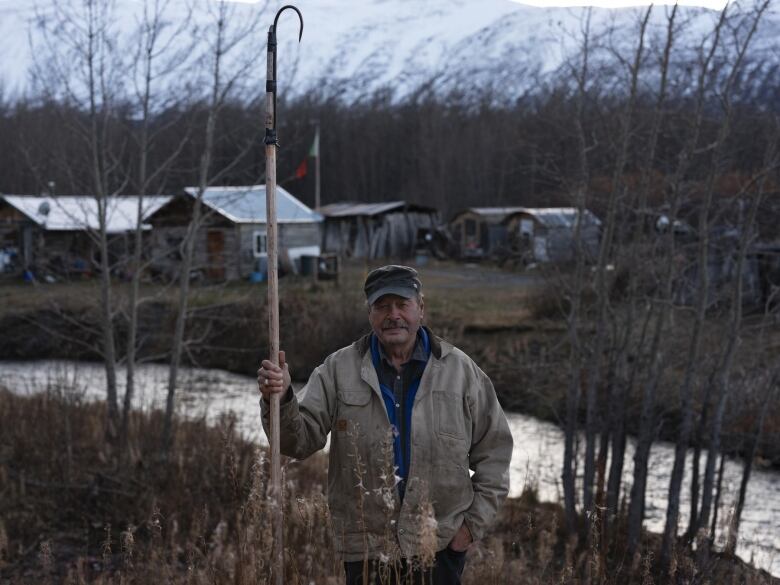 A man holds a pole in front of a creek.